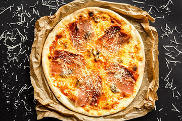 Crispy italian style pizza with prosciuto ham and artichockes, paper, cheese, dark background