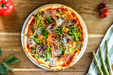 Crispy pizza with rucola and herbs served on a wooden table
