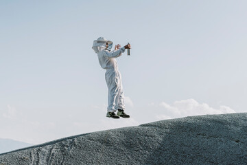 Man wearing a beekeeper dress jumping on a hill