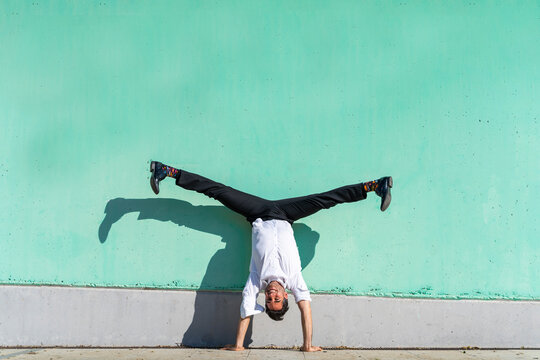 Businessman doing straddle handstand against green wall
