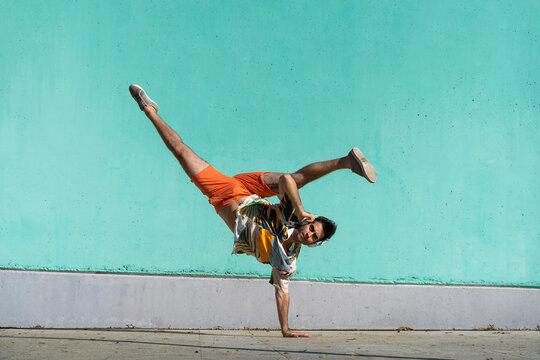 Casual man doing handspring in front of green wall