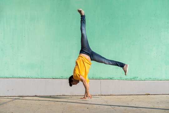 Casual man doing handspring in front of green wall
