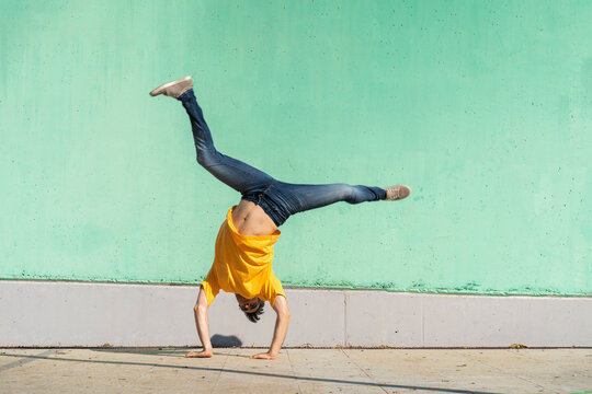 Casual man doing handspring in front of green wall