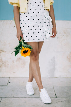 Young woman in polka dot dress holding sunflower, low section