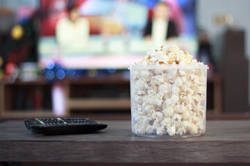 White popcorn a clear colored bowl on the table has blur remote control inside the home for eating during television viewing or as a nutrition meal during movie cinema viewing time.