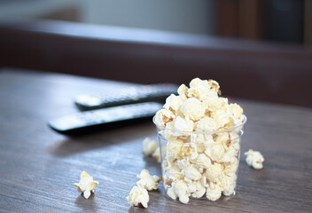 White popcorn a clear colored bowl on the table has blur remote control inside the home for eating during television viewing or as a nutrition meal during movie cinema viewing time.
