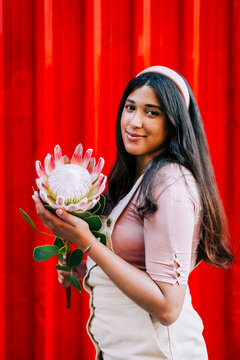 Young woman in front of red wall, holding protea flower