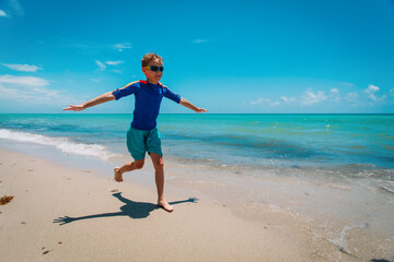 happy boy run, kid fly and play with waves on beach