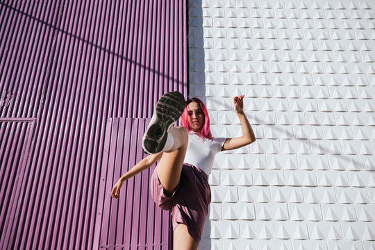Young woman with dyed red hair dancing in front of purple wall in the city