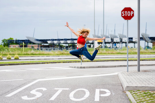 Young woman jumping mid-air in the street over stop sign