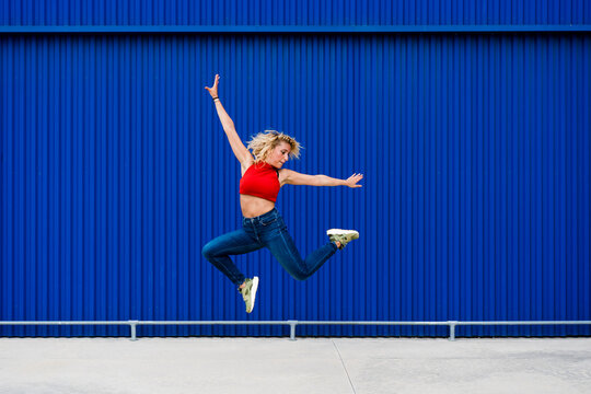Young woman jumping in front of blue wall in the city