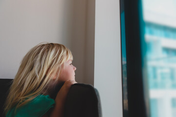 Little girl staying home, child lookint through the window outside