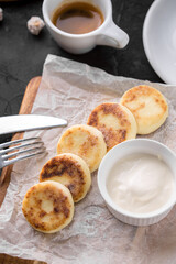 cottage cheese pancakes with sour cream sauce and cup of coffee on black table