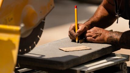 Handwerker markiert mit einem Stifft den Schnitt mit einer Kreissäge auf einer Betonplatte, Terrassenplatte.