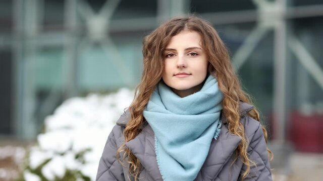 Attractive serious Face young woman looking at camera beautiful curly hair stand on street city lifestyle winter girl city outdoors.