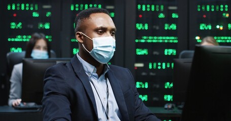 African American IT programer working on desktop computers in data center control room. Young...