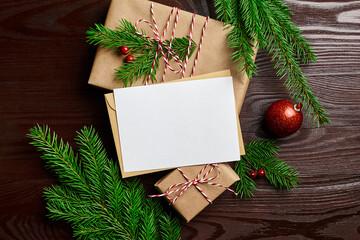 Greeting card mockup with gift box, red christmas ball and fir tree branches on wooden background
