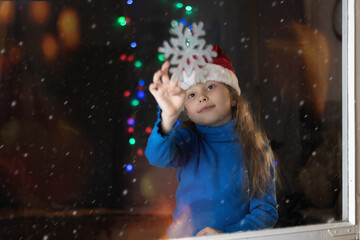 Year's table and Christmas at home, a festive atmosphere.A little girl in a Santa hat glues a snowflake to the window