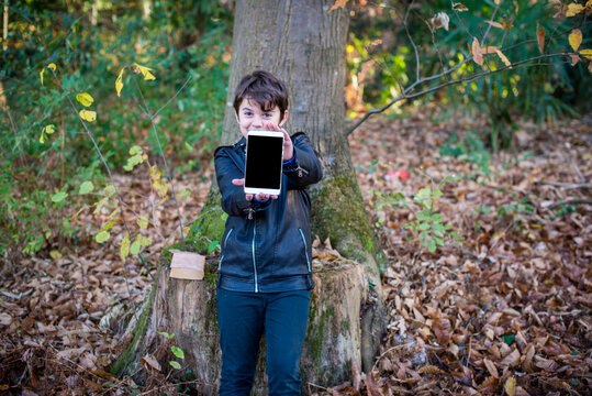 Portrait Of 11 Year Old Boy In The Nature Holding A Tablet In The Hands Shows It Smiling