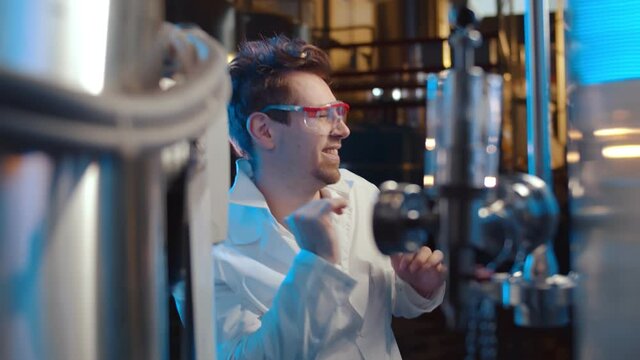 Portrait of happy scientist in white coat and goggles dancing in large industrial laboratory