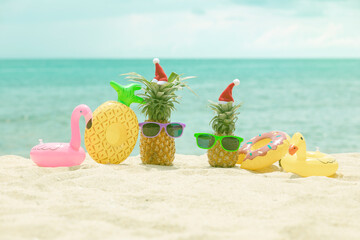 Family of funny attractive pineapples in stylish sunglasses on the sand against turquoise sea. Wearing christmas hats. Christmas and new year vacation concept on tropical beach. Family holiday. Bright