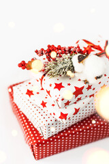 Fir branch in the snow with holly berries and gifts with a red ribbon. Gift boxes in beautiful packaging on a white background. Holiday, New Year and Christmas concept.