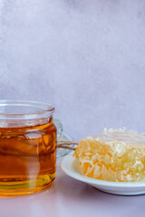 glass jar full of honey, plate with honeycomb on light brown background