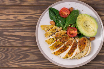 Healthy dietary salad with chicken fillet, avocado, nuts and fresh vegetables.Detox and healthy concept. Keto food. In a plate, on a wooden background.