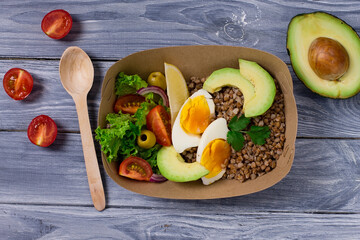 Healthy food in disposable eco-friendly food packaging. Avоcado, boiled egg, tomatoes, olives, buckwheat