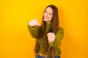 Young beautiful Caucasian woman wearing green sweater against yellow wall  imagine steering wheel...