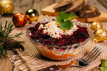 Traditional Russian herring under a fur coat in transparent plate with parsley. Rustic style.