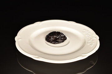 Sweet organic prunes on a white plate, close-up, on a black background.
