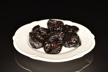 Sweet organic prunes on a white plate, close-up, on a black background.