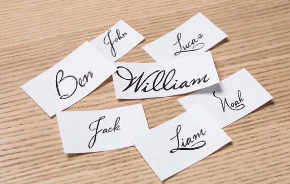 Paper sheets with written baby names on wooden table, closeup