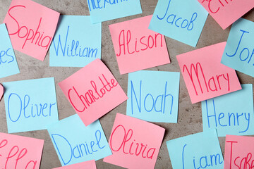 Colorful paper sheets with written different baby names on grey background, flat lay