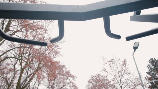 Black man in sportswear doing pull-ups on the horizontal bar with his hands. Exercising arm muscles during winter workout. Burn fat in training.