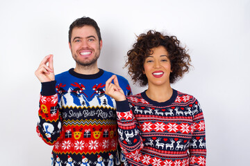 Young couple wearing Christmas sweater standing against white wall pointing up with hand showing up seven fingers gesture in Chinese sign language QĪ«.