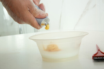 Woman preparing dye for hair coloring at white table indoors, closeup