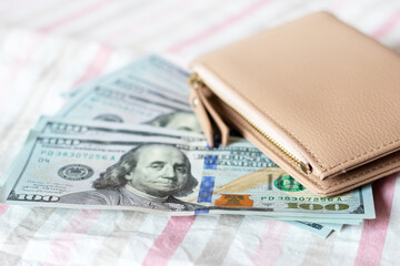 Dollars and a stylish wallet on a striped fabric