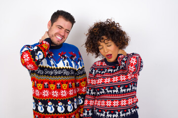 Young couple wearing Christmas sweater standing against white wall Suffering of neck ache injury, touching neck with hand, muscular pain