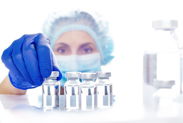 Female nurse in safety mask and gloves takes vial with liquid medicine from refrigerator shelf