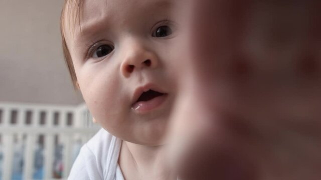 Cute baby boy trying to reach camera. Little kid looking at camera while crawling in bed 4k