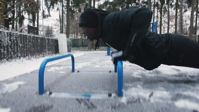 Black man doing push-ups with his hands in the winter outdoors. Weight training chest muscles. Raising body tone. Camera movement.