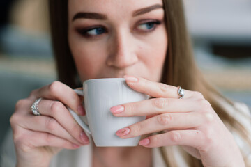 Young woman in white jacket working in cafe with papers, drinking coffee