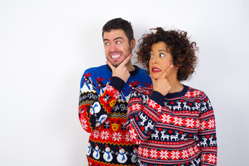 Young couple wearing Christmas sweater standing against white wall Thinking worried about a question, concerned and nervous with hand on chin.