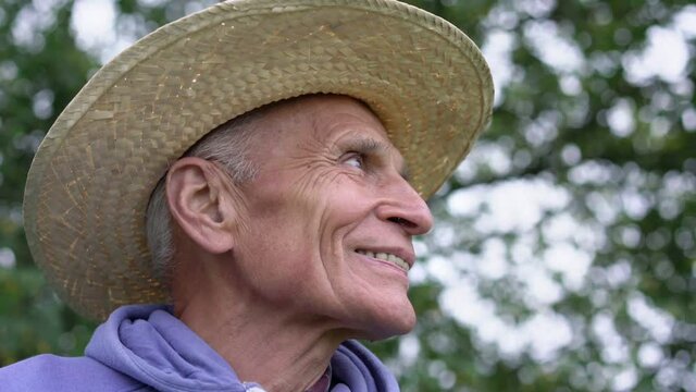 Senior happy farmer wears in big hat turns head and looks with smile and shows teeth