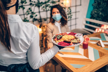 Young waitress with face protective mask working in restaurant. Coronavirus or Covid-19 concept.