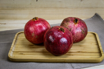 Three ripe pomegranate fruits. Red large pomegranates. Pomegranates on a wooden tray, with all the tablecloth underneath. Whole pomegranate fruit.