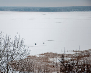 Panoramic winter top view of a huge river covered with ice and snow. Fishermen are sitting in the distance. High quality photo