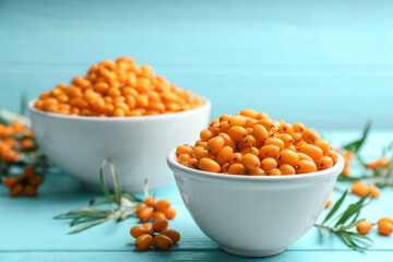 Fresh ripe sea buckthorn in bowl on light blue wooden table